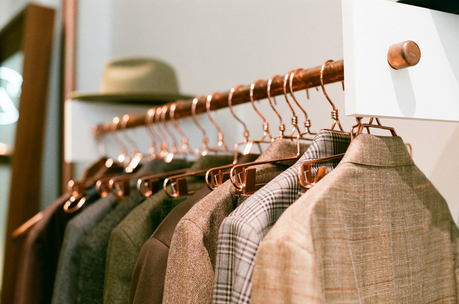 A rail of wool and tweed jackets on copper hangers in a menswear shop