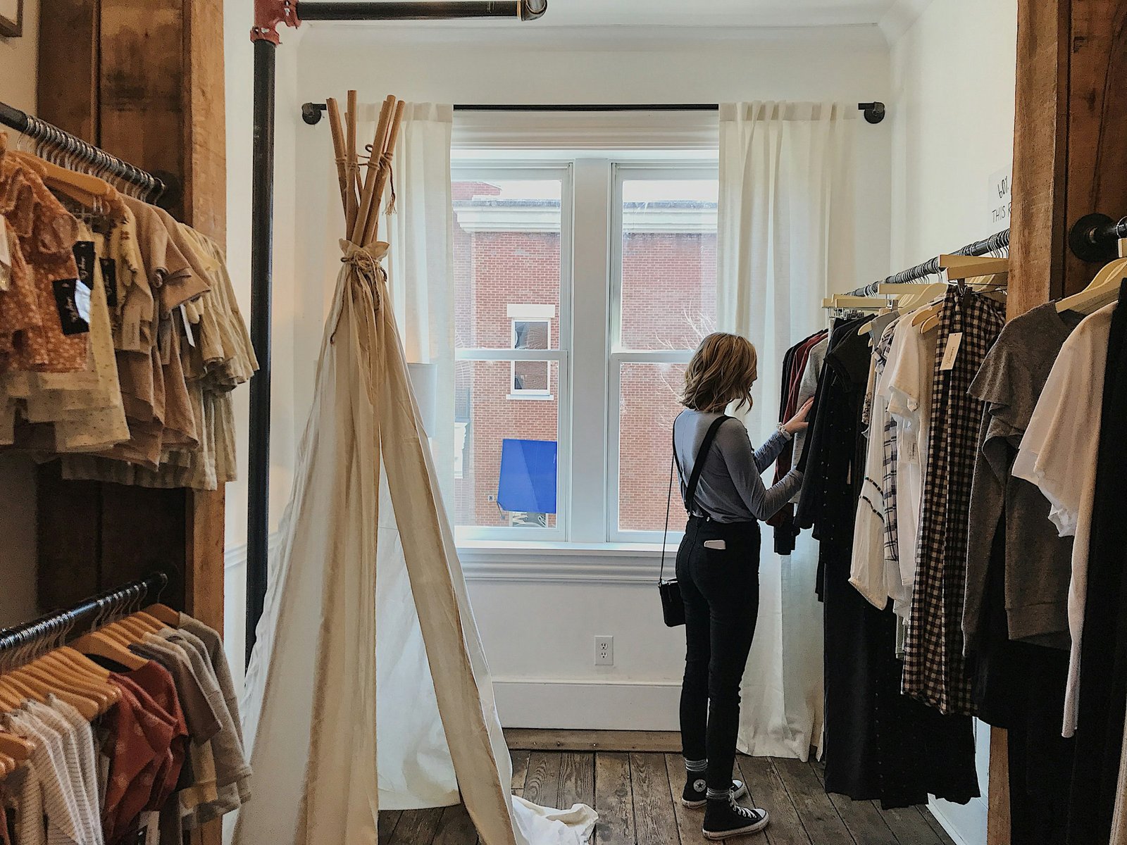 A woman going through a rail of clothes beside a window